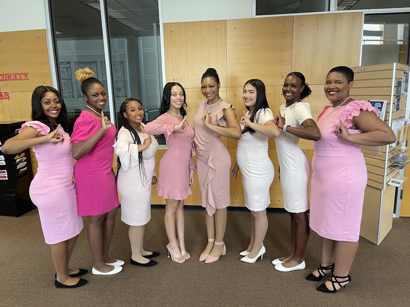 Sigma Sigma Chapter group - eight members standing in variations of pink & white dresses, giving the symbol