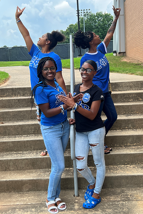 Image of four members of the Iota Sigma Chapter of Zeta Phi Beta Sorority, Inc.  posing on stairs, holding up their hand signs