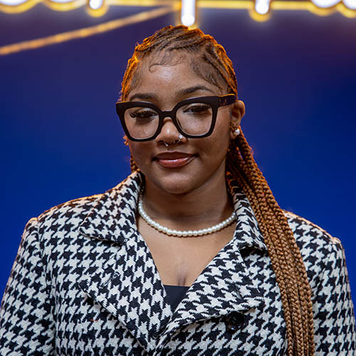 Image of Jalia Hardy, wearing a stylish black and white jacket and black framed glasses
