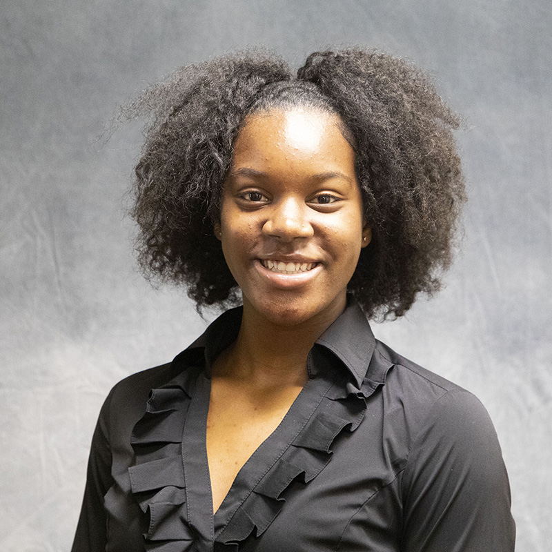 Image of Rebecca Oji wearing a black top with ruffles around the collar. 