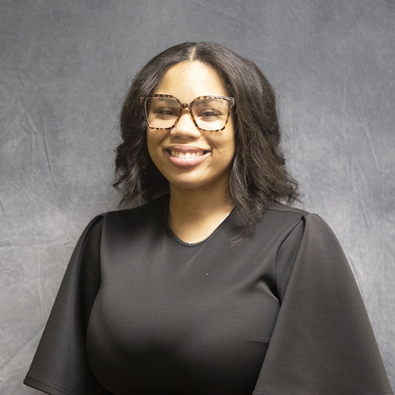 Image of Tre'Lynn Walton wearing a black dress with billowy sleeves and a pair of glasses.