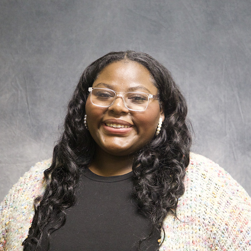 Image of Zion Rodericks wearing a white cardigan over a black shirt and glasses. 
