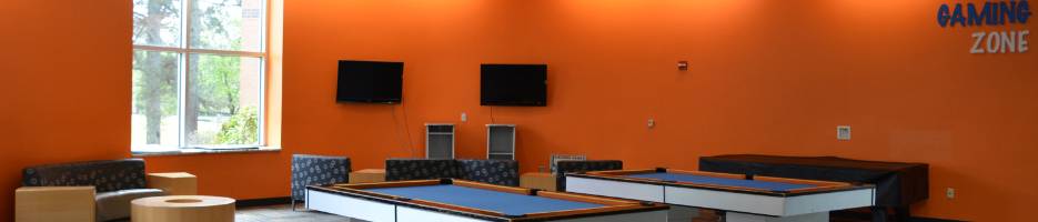 image of the gaming zone, orange wall with 'Gaming Zone' lettering, two pool tables, two large televeisions, several couches